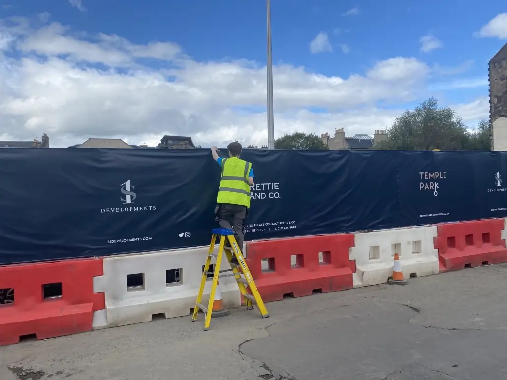 Printed site hoarding screening fitted along a construction perimeter with a surveyor working in front