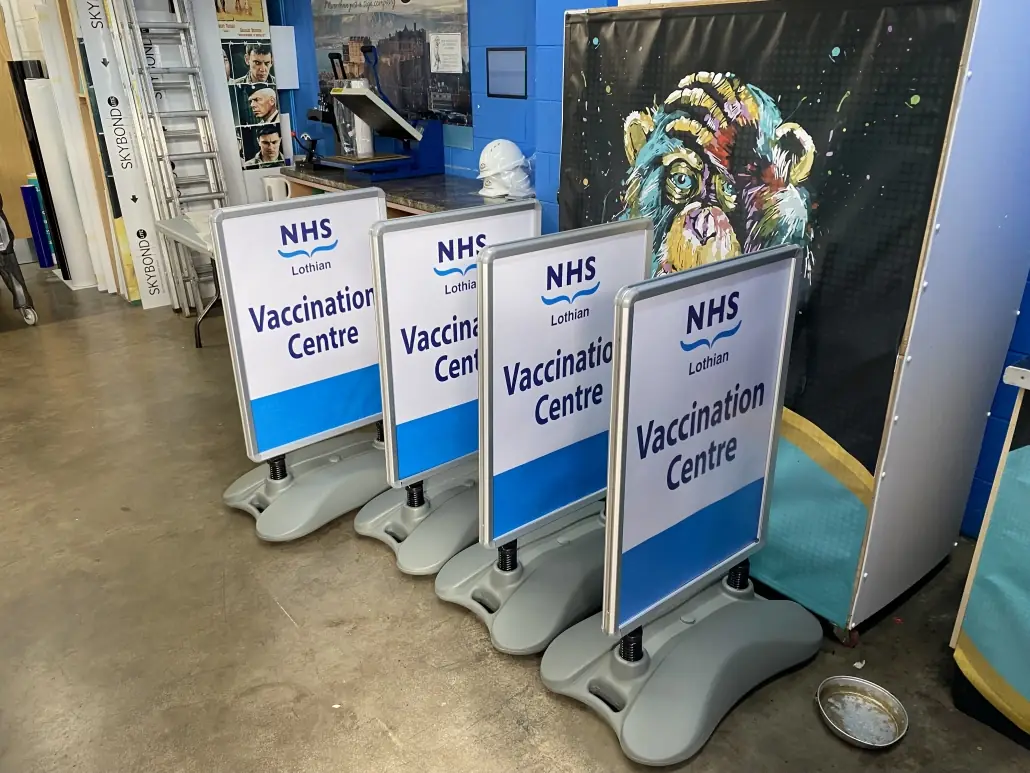 A row of printed NHS Lothian Vaccination Centre forecourt sign boards in weighted frames